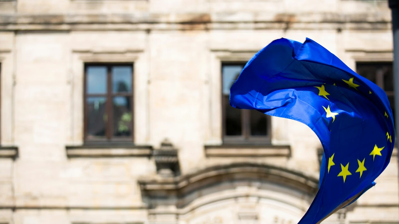 European Union flag with yellow stars waving in the wind in front of a historic European government building, symbolizing EU policy and Schengen visa regulations.