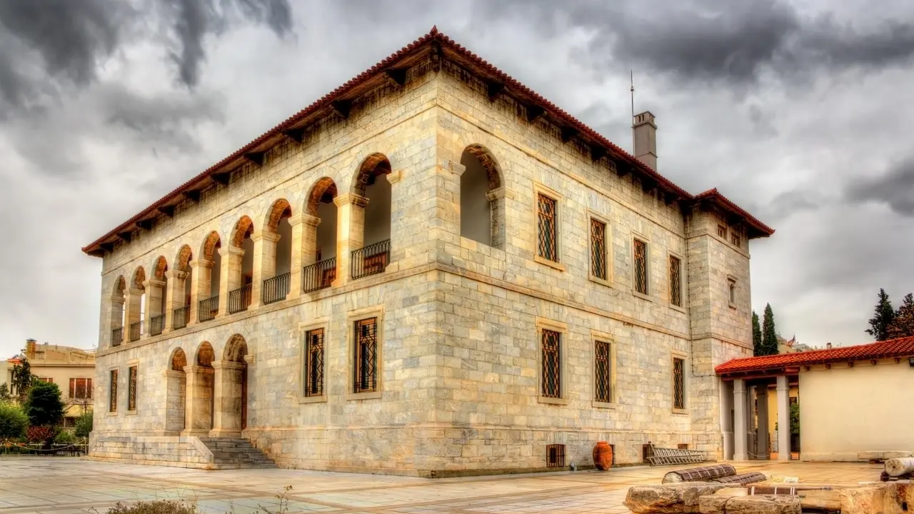 Historic stone mansion with arched colonnade and red tile roof under dramatic cloudy sky, showcasing traditional Mediterranean architecture and ornate iron window grilles.