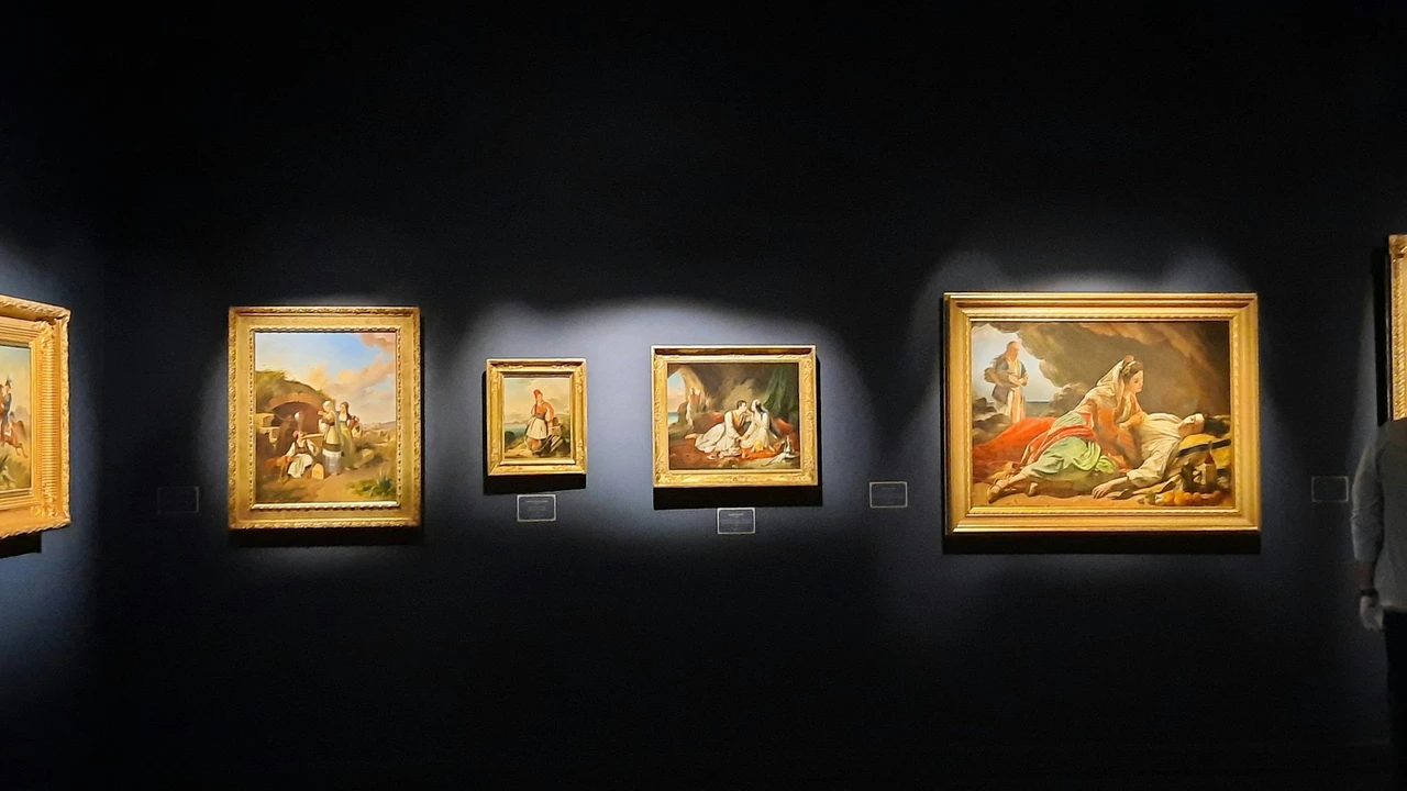 Dark museum gallery wall with spotlit, gold-framed classical paintings arranged in a row; varying sizes depict historical scenes, with a visitor partially visible at right.