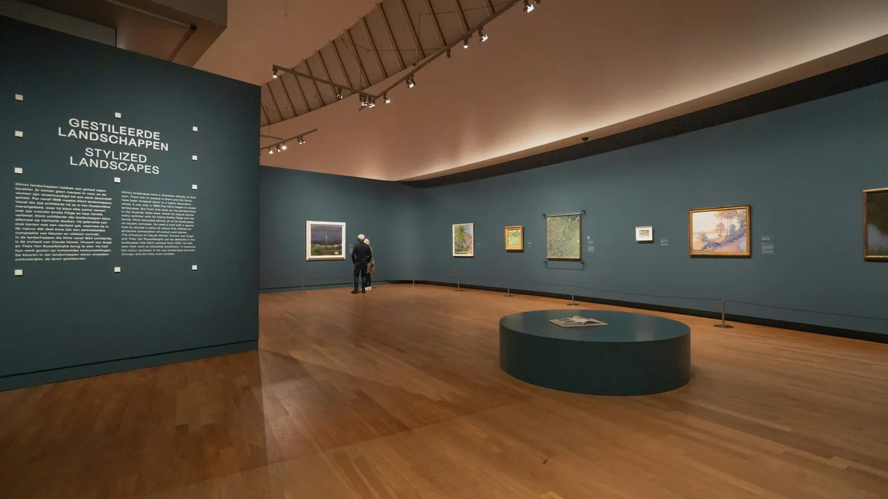 Interior of the Van Gogh Museum in Amsterdam showcasing the “Stylized Landscapes” gallery, with framed paintings displayed on blue walls, wooden floors, and visitors viewing post-impressionist artwork.