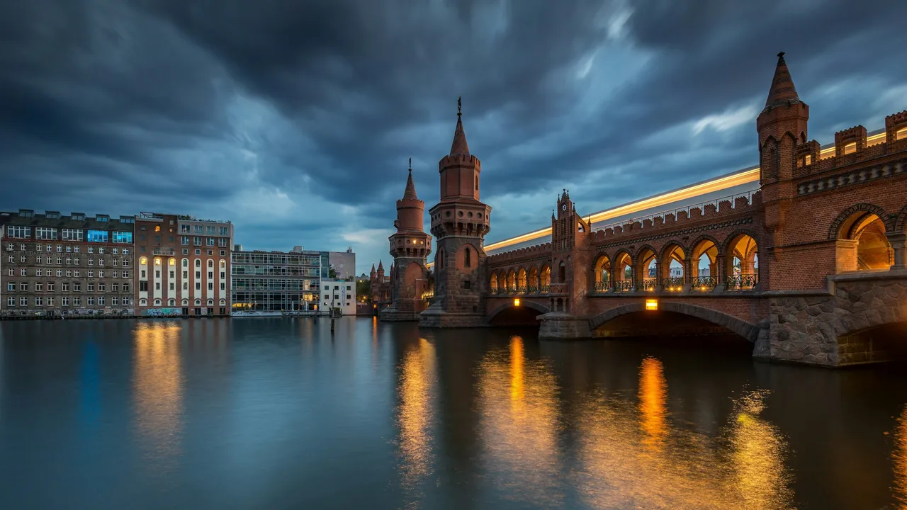 Oberbaum Bridge in Berlin at dusk with dramatic clouds reflecting on the Spree River, connecting Friedrichshain and Kreuzberg near the East Side Gallery, a famous landmark of Berlin’s historic architecture.