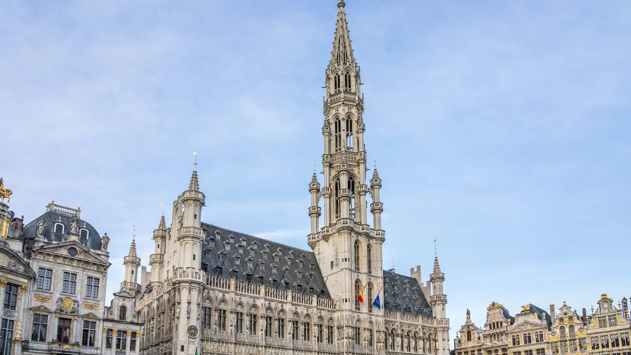 Brussels Town Hall at Grand Place featuring ornate Gothic architecture and tall central spire under a cloudy sky