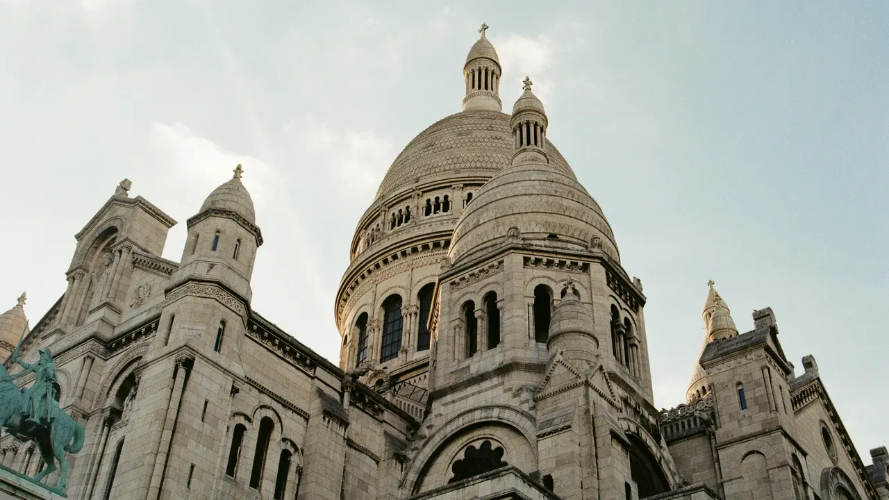 Sacré-Cœur Basilica in Montmartre, Paris, showcasing its iconic white stone domes, Roman-Byzantine architecture, and historic hilltop landmark against a clear sky.