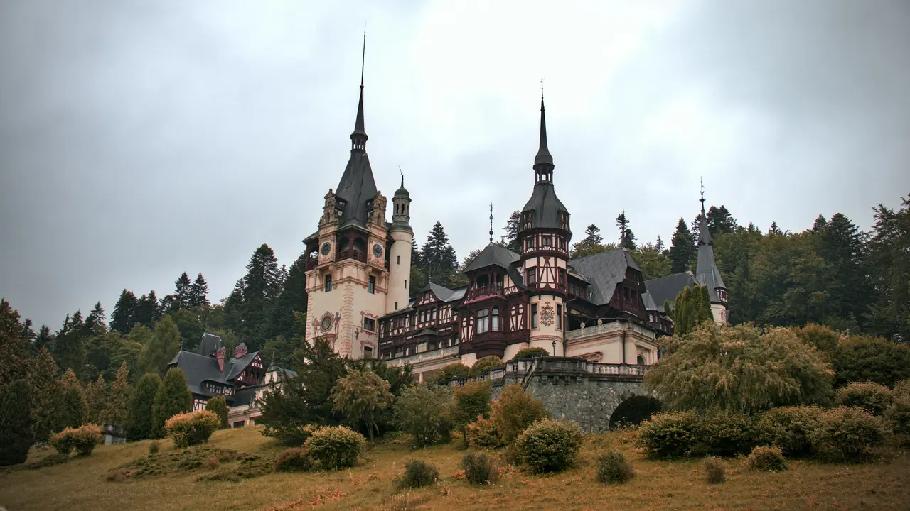 Peles Castle in Sinaia Romania with ornate Neo Renaissance architecture and tall spires surrounded by forested Carpathian Mountains under cloudy sky
