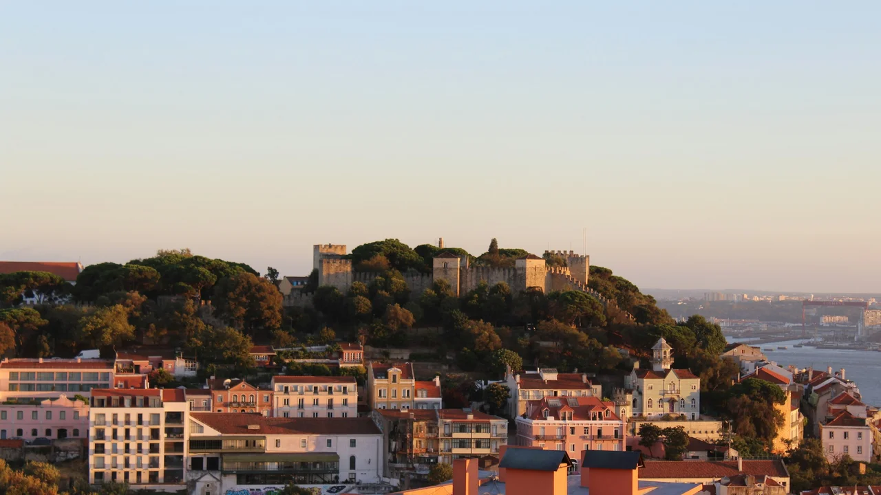 Explore São Jorge Castle in Lisbon featuring hilltop medieval fortress overlooking Alfama neighborhood, colorful historic buildings, and panoramic city views at sunset, Portugal