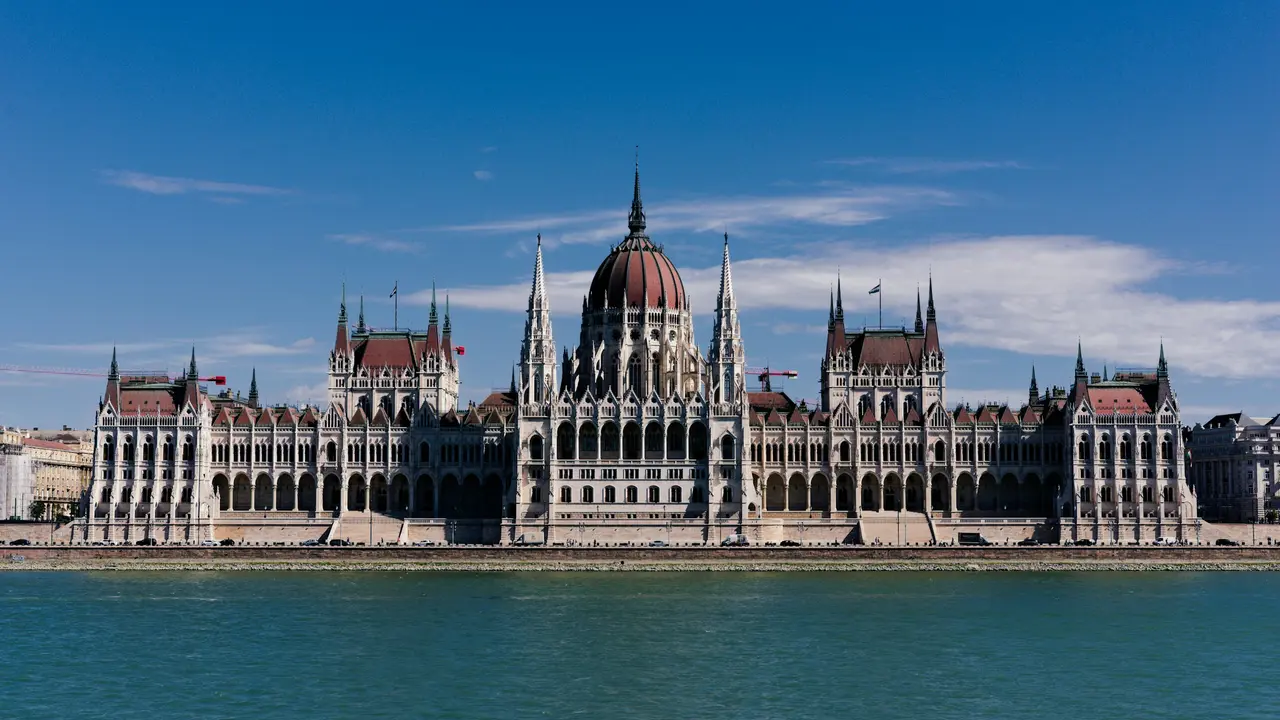 Hungarian Parliament Building in Budapest, Hungary, showcasing its iconic neo-Gothic architecture along the Danube River under a clear blue sky.