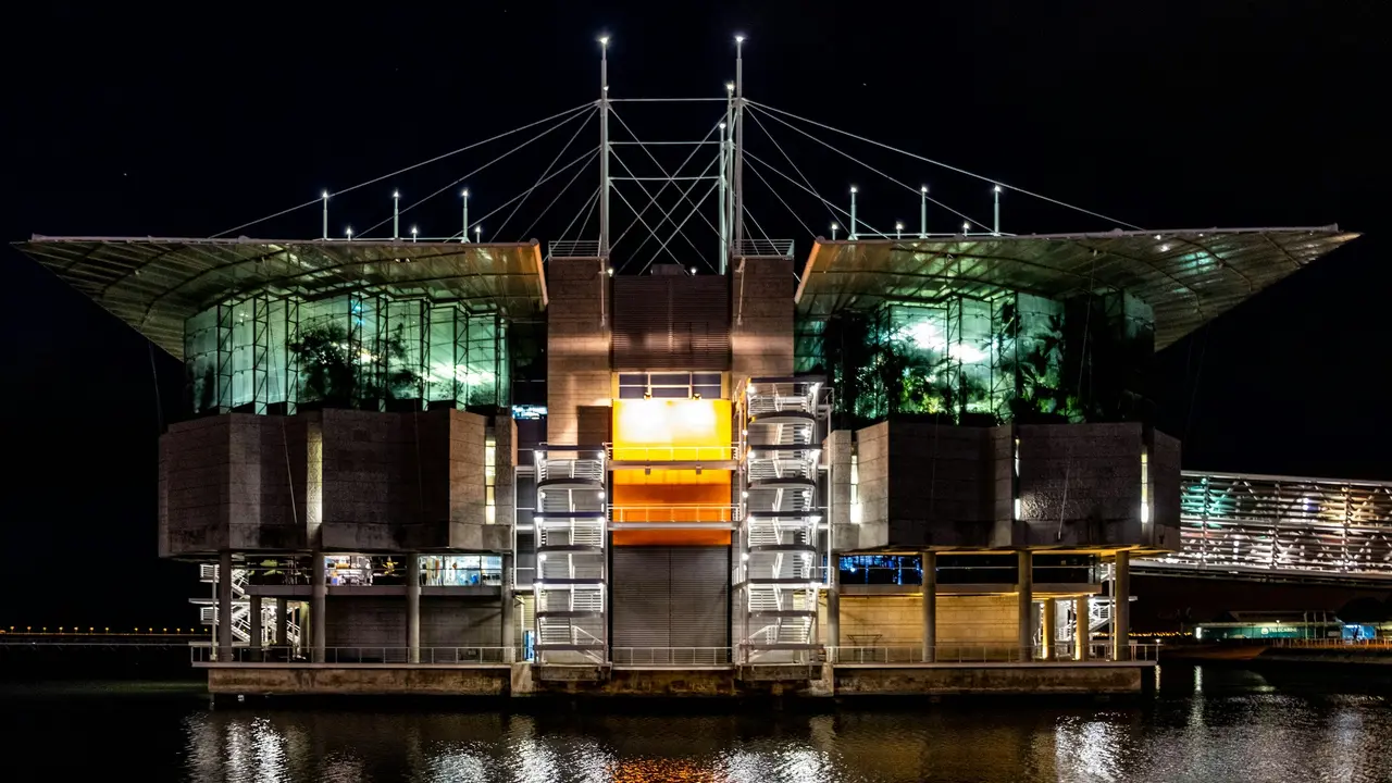 Night view of the Lisbon Oceanarium illuminated over the Tagus River, showcasing modern architecture and glass facades, one of Lisbon’s top attractions in Portugal.