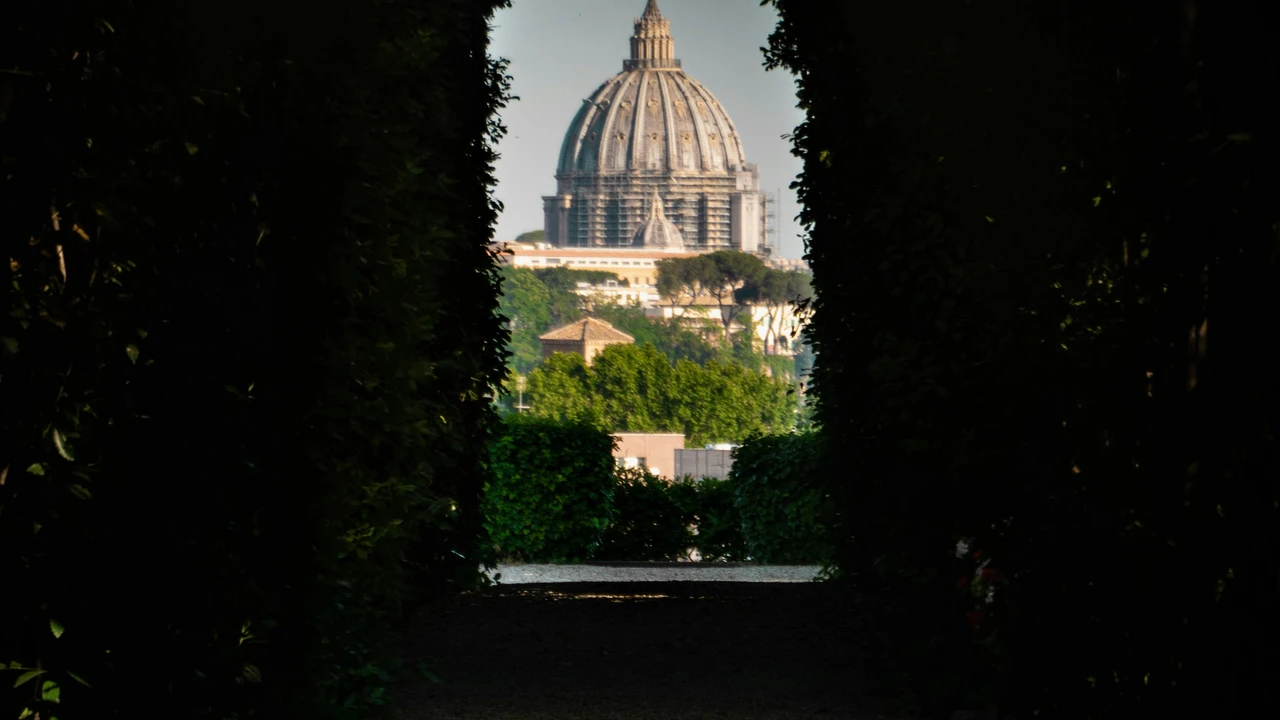 View of St. Peter’s Basilica dome perfectly framed through the Aventine Keyhole in Rome, surrounded by lush greenery along the Knights of Malta garden pathway.