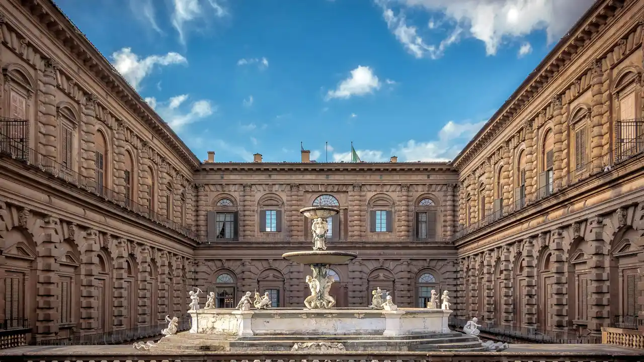 Renaissance courtyard with ornate stone architecture and central marble fountain under blue sky at Pitti Palace Florence Italy