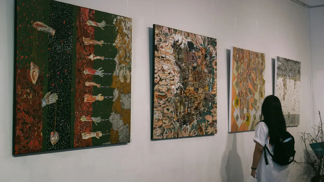 Visitor viewing large contemporary abstract paintings displayed on a white gallery wall in a modern art exhibition, showcasing colorful mixed-media artworks in a museum setting.