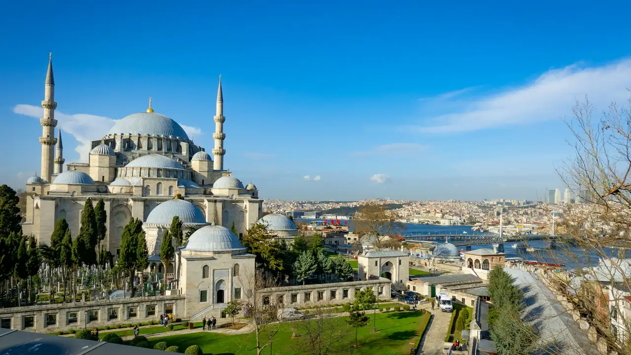 Panoramic view of the Suleymaniye Mosque overlooking the Golden Horn in Istanbul, Turkey, featuring grand Ottoman domes, tall minarets, landscaped gardens, and a clear blue sky