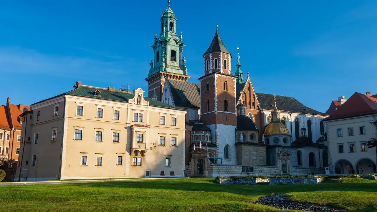 Wawel Royal Castle complex in Kraków, Poland, featuring historic cathedral towers, Renaissance and Gothic architecture, and green lawns under a clear blue sky.