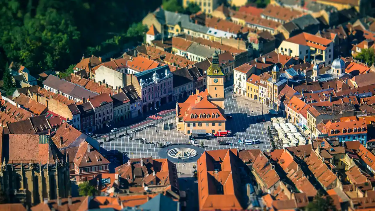 Aerial view of Brasov Council Square in Romania featuring colorful old town buildings, red tiled roofs and historic clock tower in Transylvania