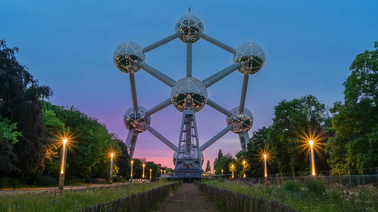Atomium in Brussels illuminated at sunset with glowing spheres and park pathway leading to the iconic Belgian landmark