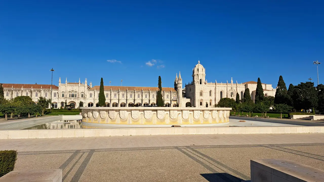 Visit the Jerónimos Monastery in Lisbon showcasing the iconic Manueline architecture, historic monastery facade, ornamental fountain, and clear blue sky in Belém, Portugal