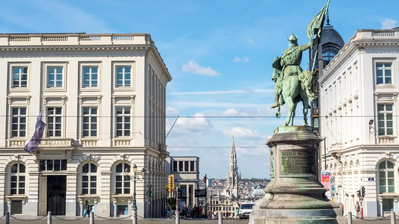 Equestrian statue in Brussels city center with historic neoclassical buildings and Mont des Arts skyline under blue sky, showcasing Belgium travel landmark and European architecture.