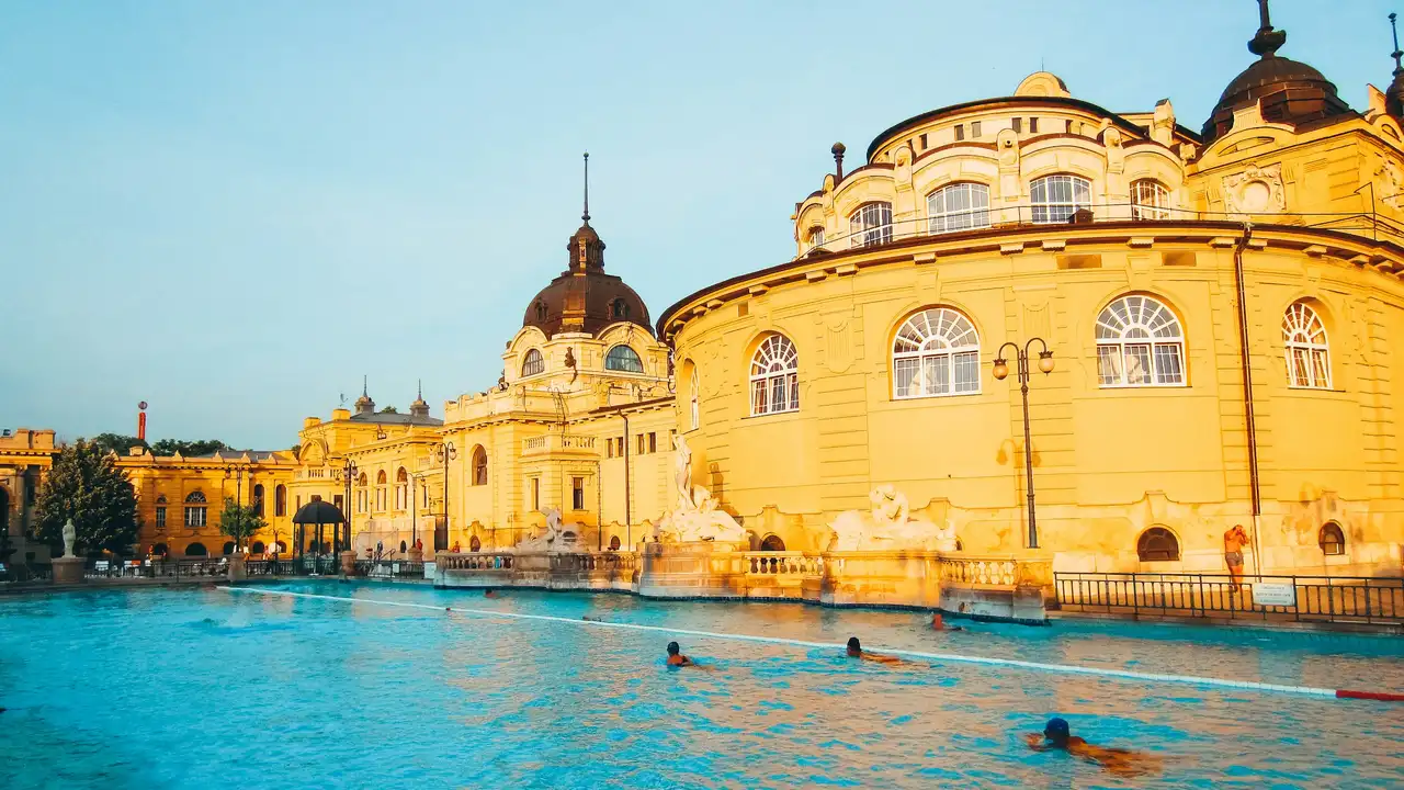Széchenyi Thermal Bath in Budapest, Hungary, featuring historic yellow neo-Baroque buildings and outdoor thermal pools with visitors relaxing in the water.