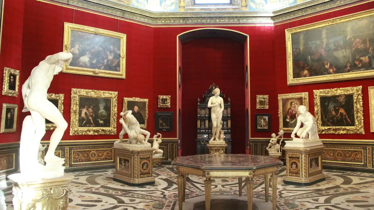 Interior of the Gallerie dell’Accademia in Venice featuring classical marble statues, Renaissance paintings in ornate gold frames, and a richly decorated red-walled museum gallery.