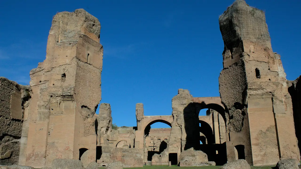 Ancient ruins of the Baths of Caracalla in Rome, showcasing massive brick walls, arches, and remnants of Roman bathhouse architecture under a clear blue sky.
