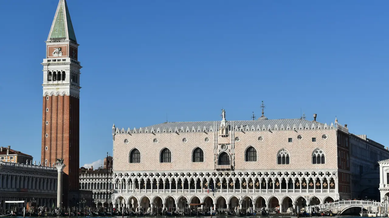 Doge’s Palace (Palazzo Ducale) in Venice, Italy, with its Gothic façade, ornate arches, and the Campanile of St. Mark’s Square under a clear blue sky.