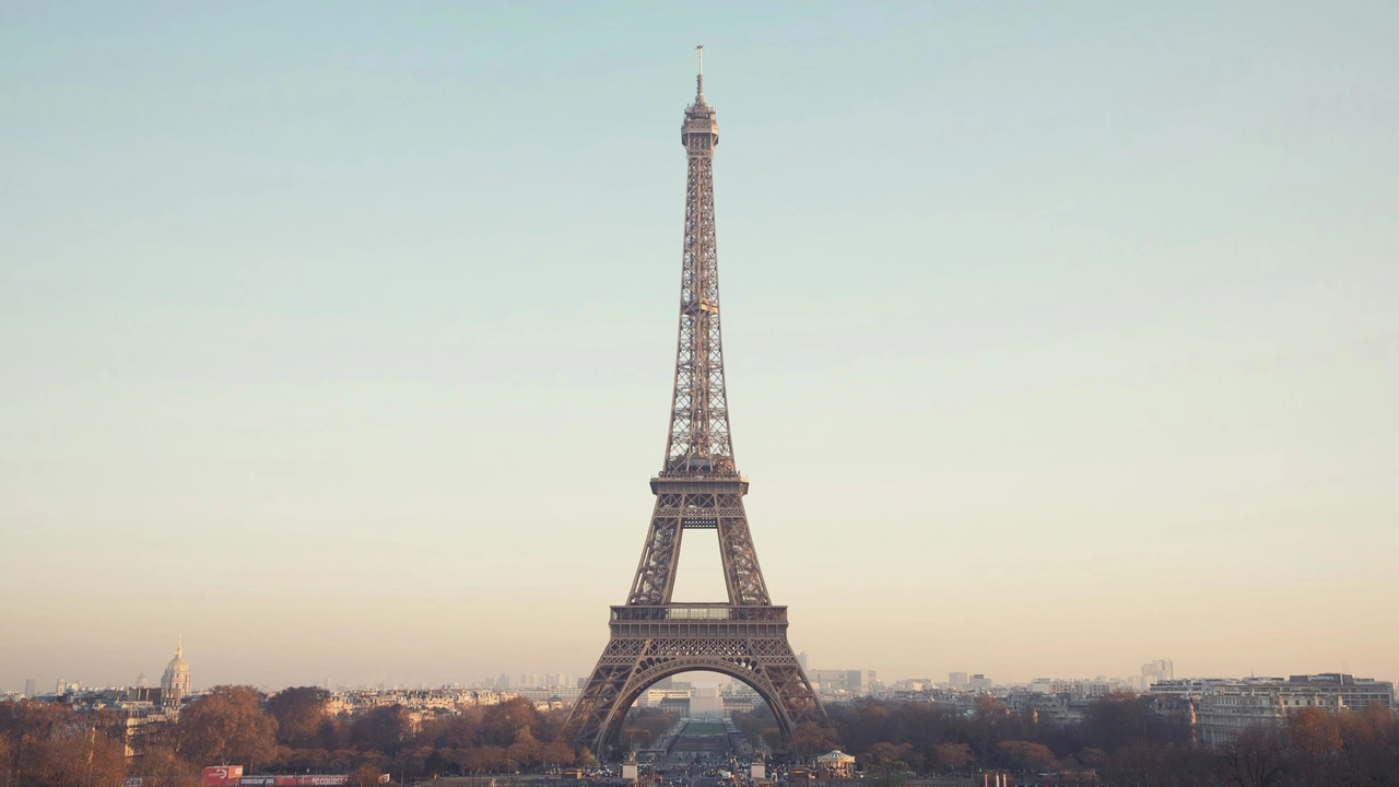 The Eiffel Tower in Paris standing tall above the city skyline, viewed from the Champ de Mars with a clear sky and historic buildings in the background.