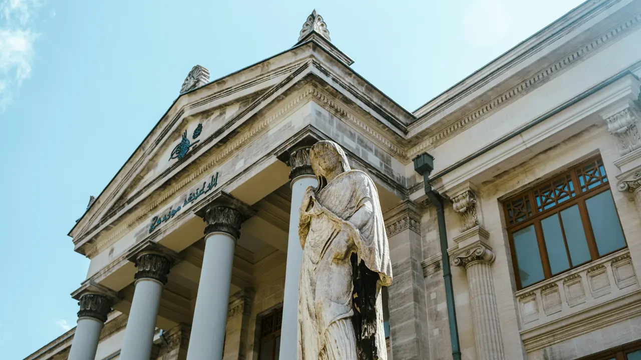 Neoclassical courthouse building with tall Corinthian columns and marble statue in front under blue sky