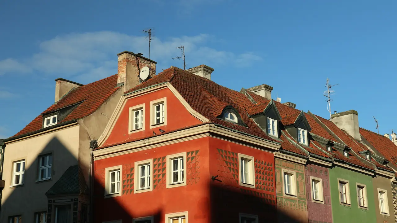 Colorful historic townhouses in Kraków, Poland, featuring traditional red-tiled roofs, pastel facades, and classic European architecture under a clear blue sky.