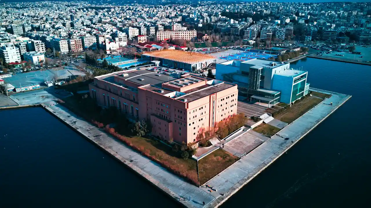 Aerial view of the Archaeological Museum of Thessaloniki on the waterfront, surrounded by modern buildings and the city skyline.