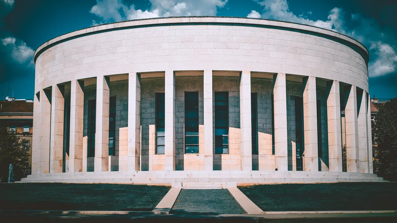 A low-angle shot of the Museum of Broken Relationships in Zagreb, featuring its distinct circular white stone architecture and pillars under a blue sky