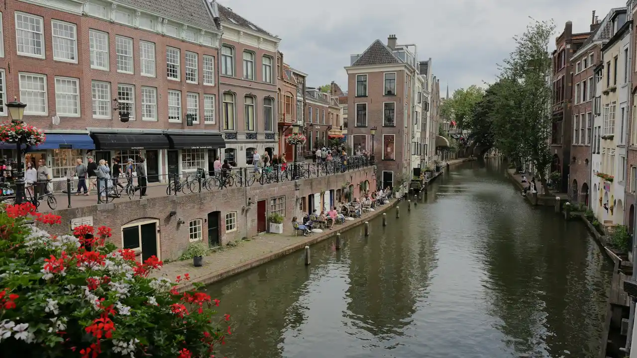 Historic Utrecht canal with traditional Dutch brick houses, waterfront cafes, bicycles, and pedestrians along Oudegracht in the Netherlands