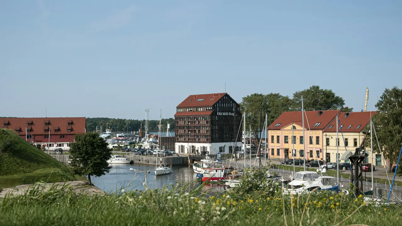Scenic harbor view in Klaipėda, Lithuania, featuring historic waterfront buildings, marina boats, and the Old Mill Hotel, representing life and residency opportunities in Lithuania for permanent residence permit applicants.