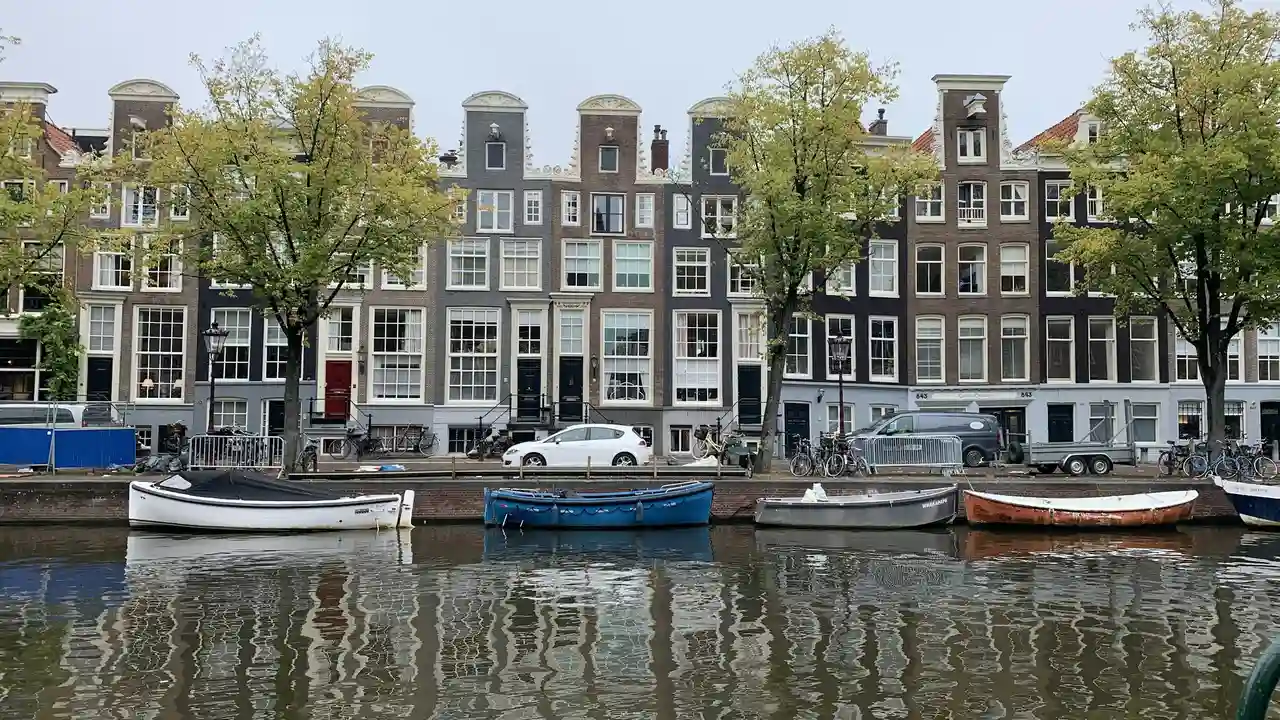 Amsterdam canal houses with gabled facades, moored boats, and tree lined waterfront in the Netherlands