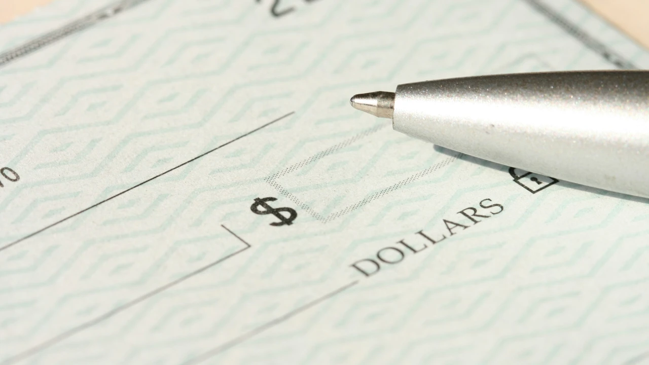 Close-up of a pen resting on a bank check showing a dollar sign and amount field, symbolizing payment of visa application fees or financial documentation.