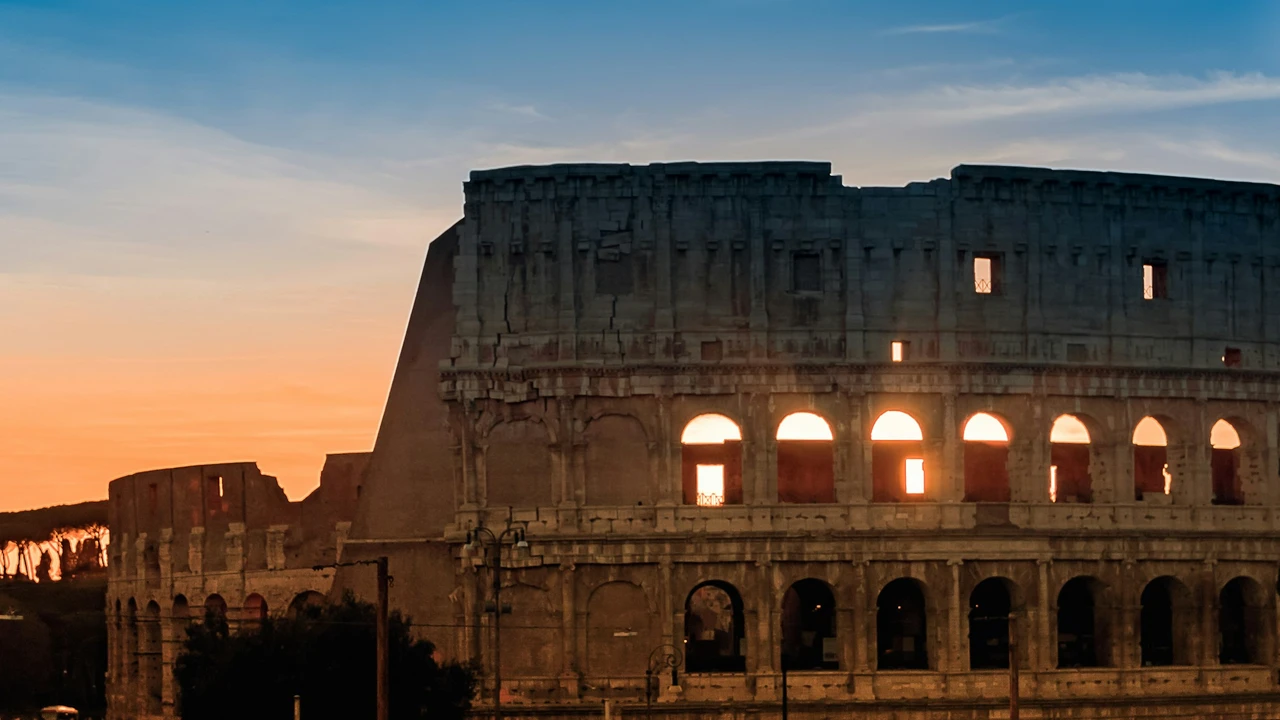 “The Colosseum in Rome, Italy at sunset with golden sunlight shining through ancient arches, iconic Roman landmark and popular tourist attraction.