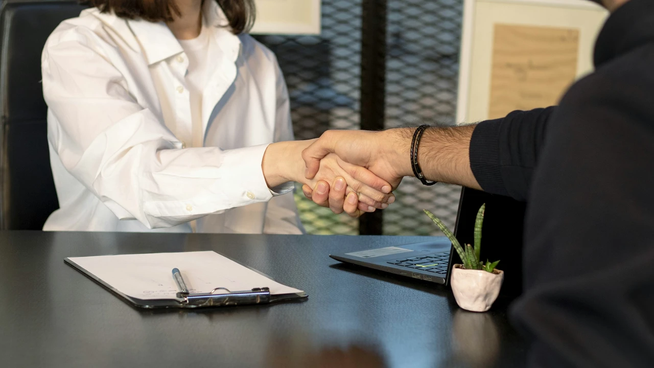 Job interview handshake between employer and candidate across a desk with documents and laptop, symbolizing successful interview, hiring decision, and employment agreement.