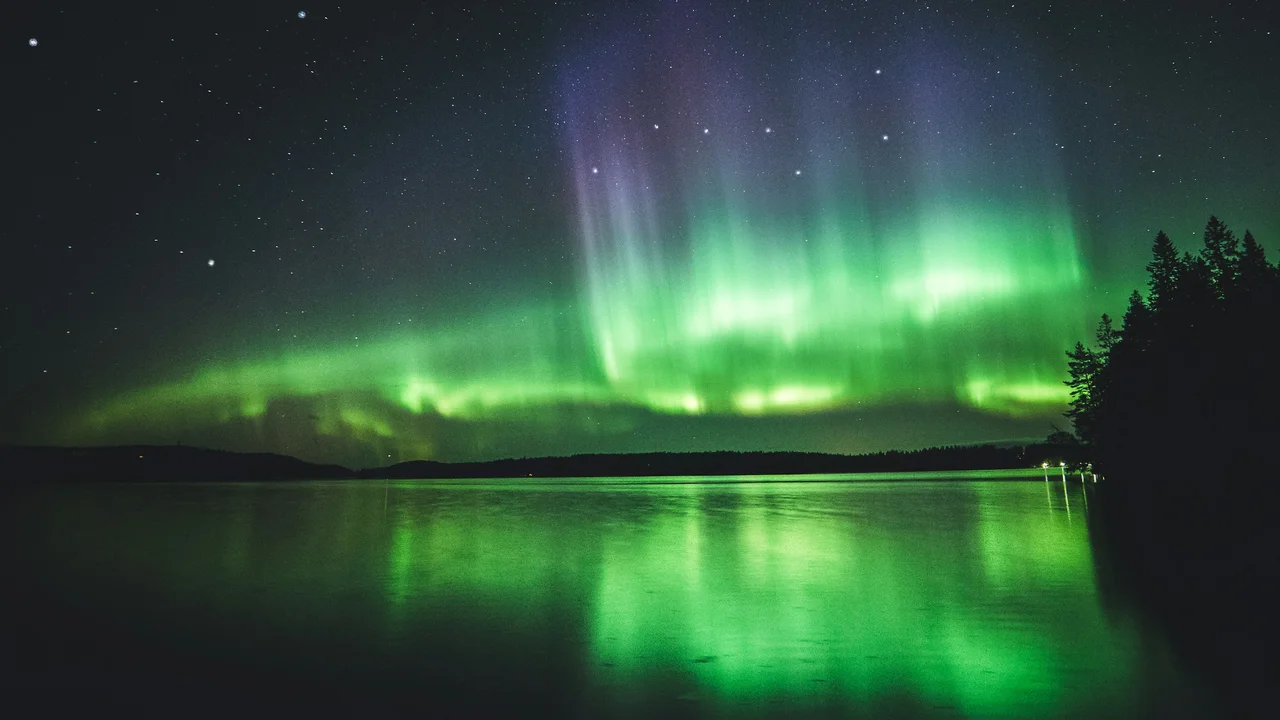 Aurora Borealis over a calm lake in Finland, with green and purple northern lights reflecting on water, symbolizing Nordic travel, Finland tourism, and visa-related journeys.