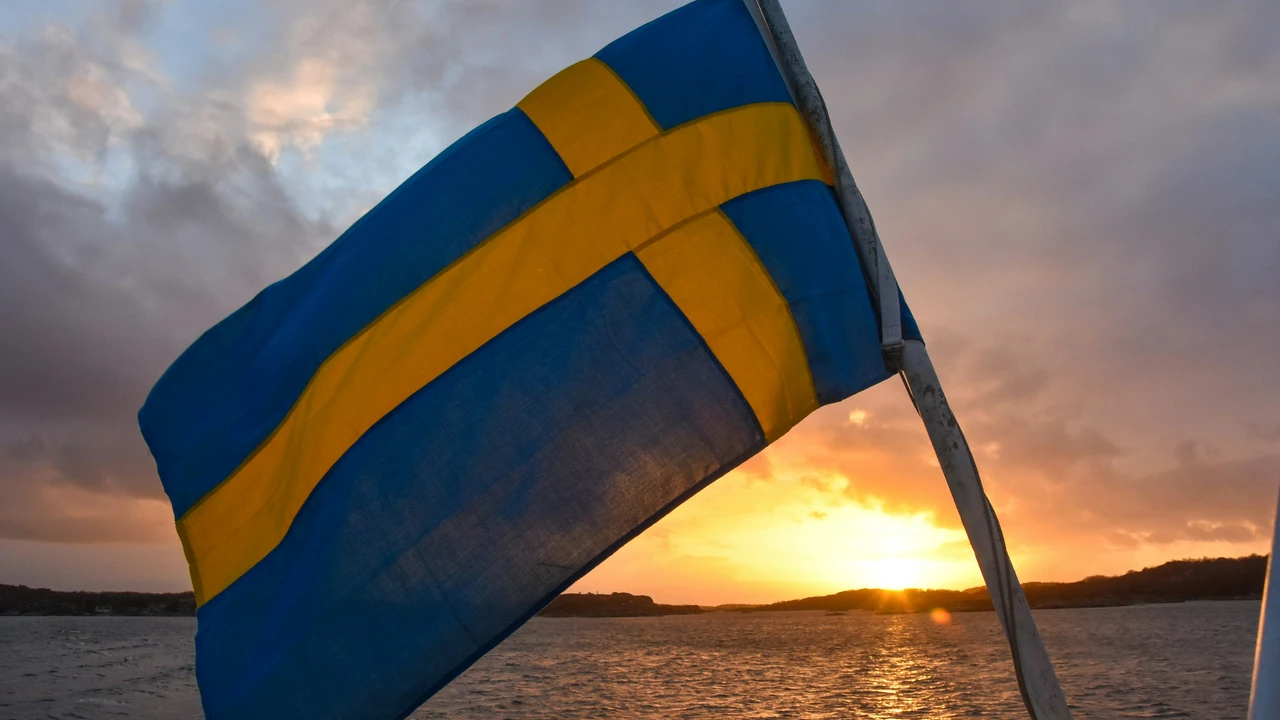 Swedish national flag waving over the sea at sunset, symbolizing Sweden travel, tourism, and visa requirements, with golden sunlight reflecting on coastal waters.