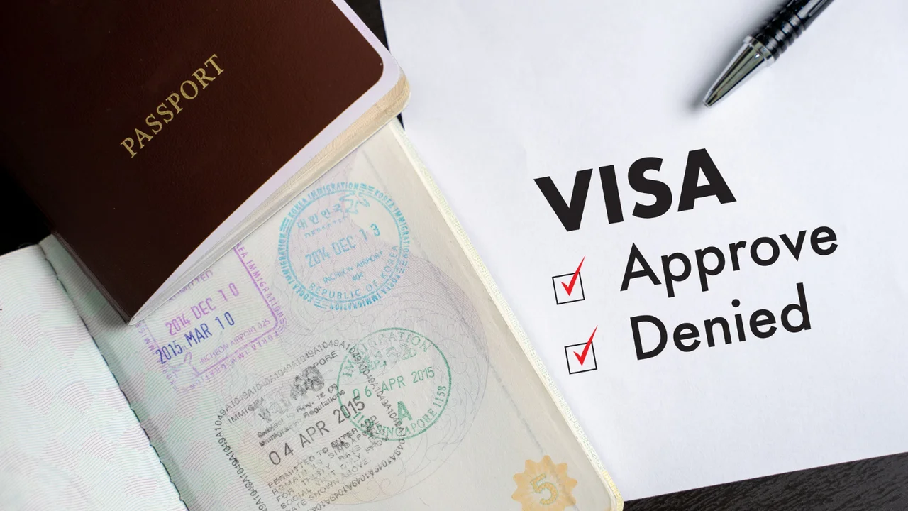 Open passport with immigration stamps next to a visa application form showing “Approved” and “Denied” options checked, symbolizing travel visa approval or rejection process.