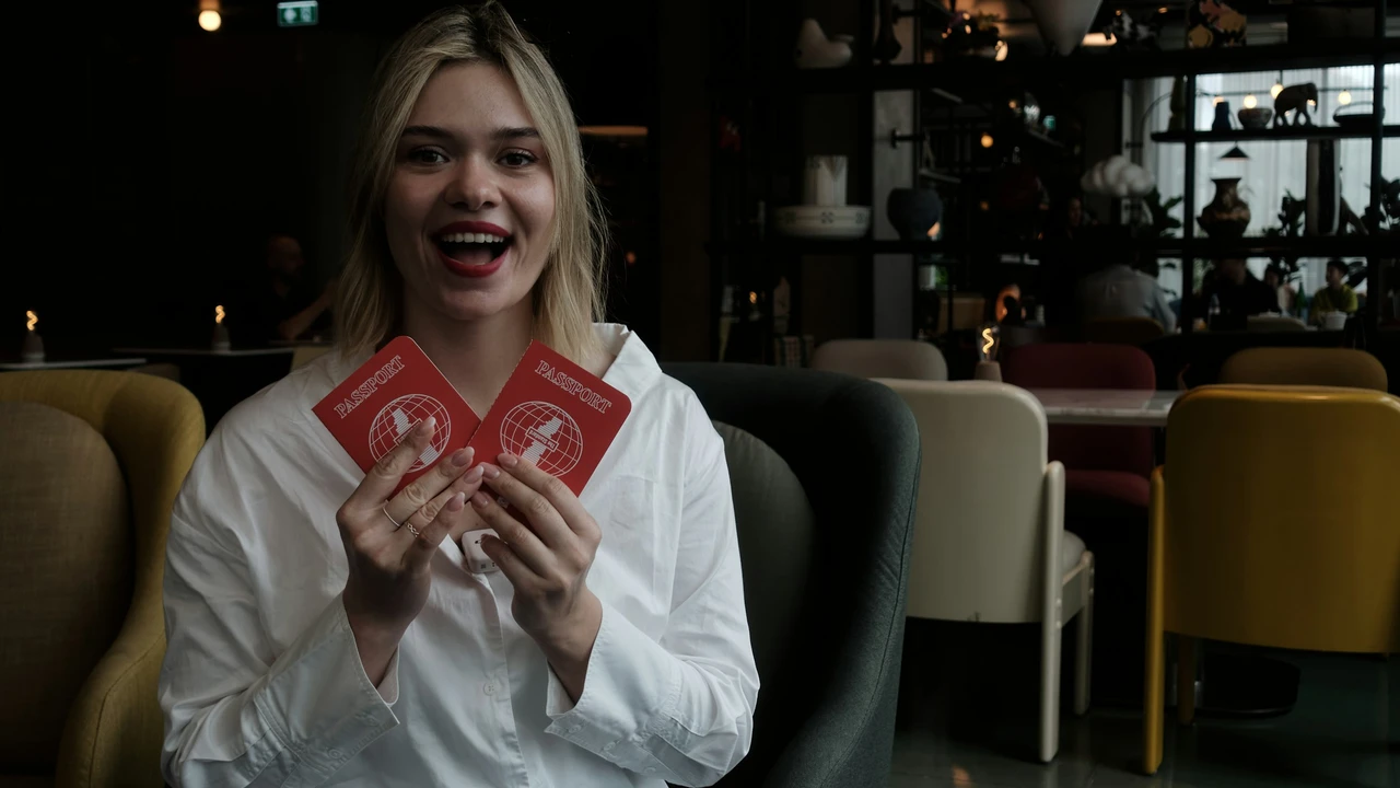 Smiling traveler holding two passports inside a modern café, representing eligibility and requirements for applying for a Luxembourg visit visa.