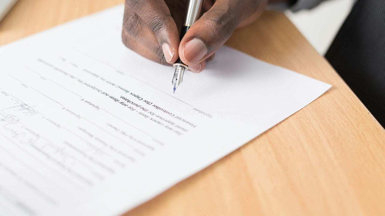 A close-up shot of a person's hand using a fountain pen to sign a formal document on a wooden desk. The focus is on the tip of the pen as it makes contact with the signature line of the paper, which contains printed text and multiple signature fields