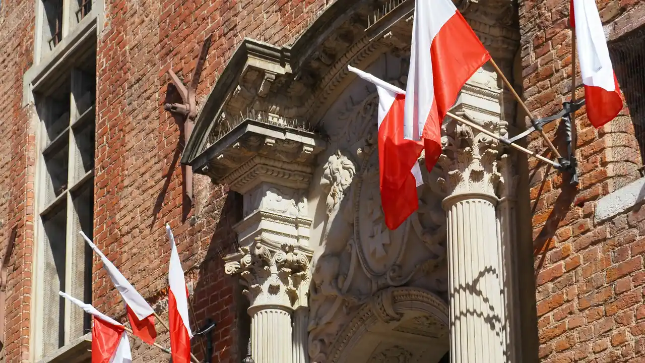 Polish national flags hanging on a historic brick building facade, showcasing traditional architecture and national heritage of Poland.