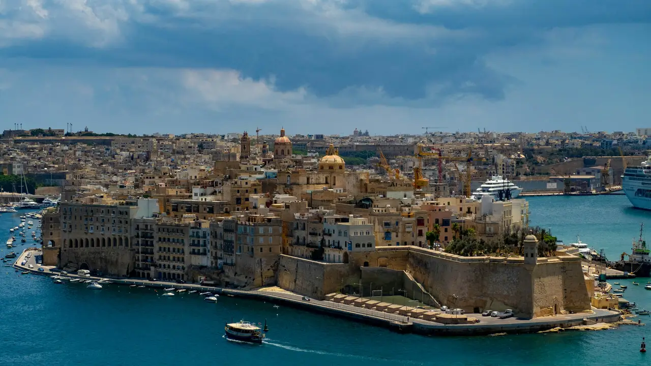 Panoramic view of Valletta, the capital city of Malta, featuring historic limestone buildings, fortified city walls, harbor waterfront, and Mediterranean coastline.