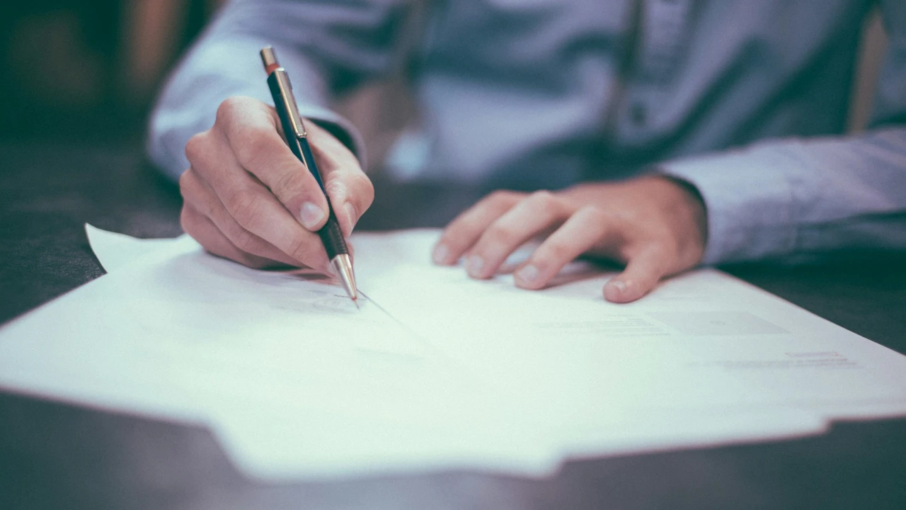 Close-up of a person signing a visa application form with a pen on a desk, representing immigration paperwork, official documentation, and travel visa approval process.