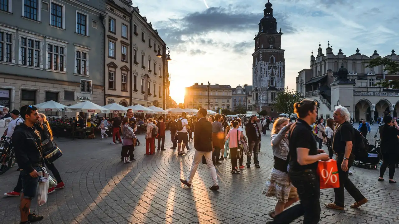 Crowds at Kraków Main Market Square (Rynek Główny) at sunset, with historic buildings, St. Mary’s Basilica tower, and lively city atmosphere in Poland.