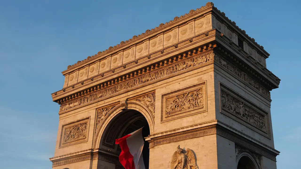 Arc de Triomphe monument in Paris, France, with the French national flag displayed, showcasing historic architecture and a famous Paris landmark under a clear blue sky.
