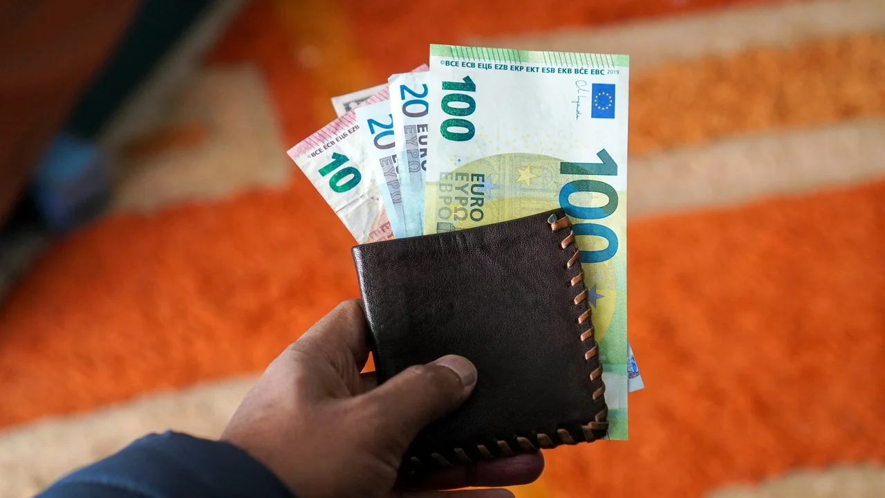 Hand holding a brown leather wallet with €10, €20, and €100 euro banknotes, representing travel expenses and visa costs for Lithuania or Europe from Nigeria.