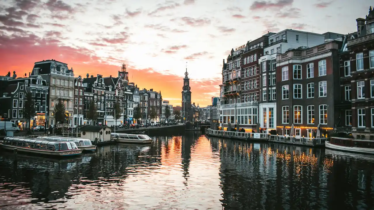 Canal view of Amsterdam at sunset with historic buildings and boats, illustrating the cost of living in the Netherlands and lifestyle in Dutch cities.