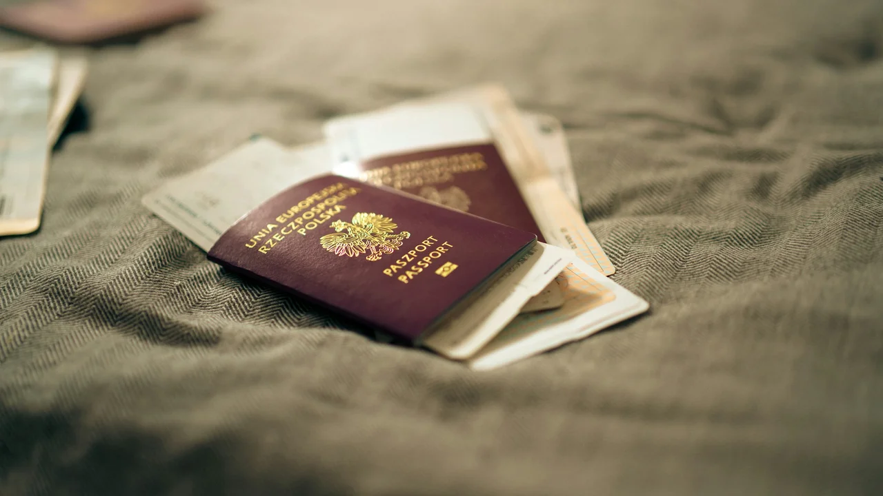 A close-up, slightly high-angle shot of a maroon Polish passport resting on a textured, grey fabric surface. The passport is emblazoned with the Polish national eagle emblem and the words