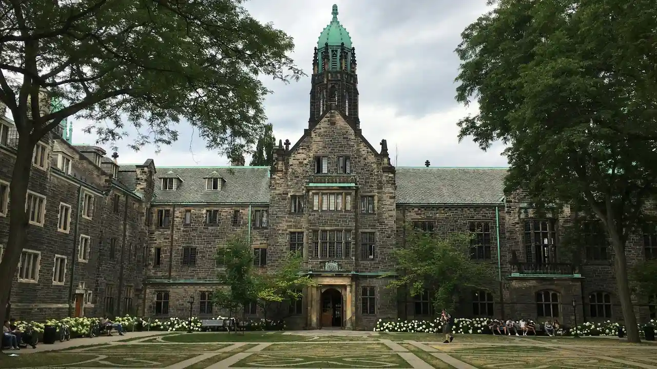 Historic McGill University campus building in Montreal, Canada, featuring a Gothic stone façade, central tower, green courtyard, and students relaxing outdoors.