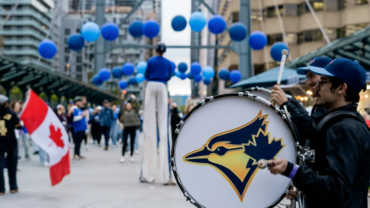 Street cultural celebration in Canada featuring a marching drummer, people holding a Canadian flag, blue balloons overhead, and urban city buildings in the background, representing Canadian culture and community events.